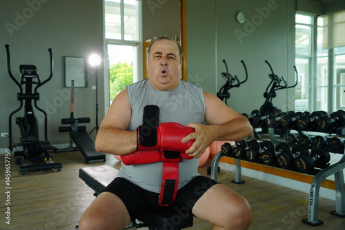 Elderly Caucasian man with a fat belly wearing gym clothes wearing red gloves practicing boxing and punching doing exercises for health and lose weight in a fitness centere.