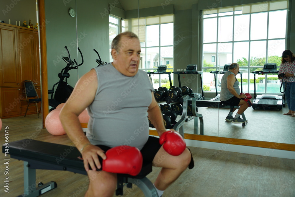 Elderly Caucasian man with a fat belly wearing gym clothes wearing red gloves practicing boxing and punching doing exercises for health and lose weight in a fitness centere.