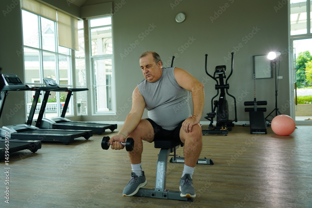 Elderly Caucasian man with a fat belly wearing gym clothes lifting dumbbells doing exercises to build muscle for health and lose weight in a fitness center Health and wellness concept
