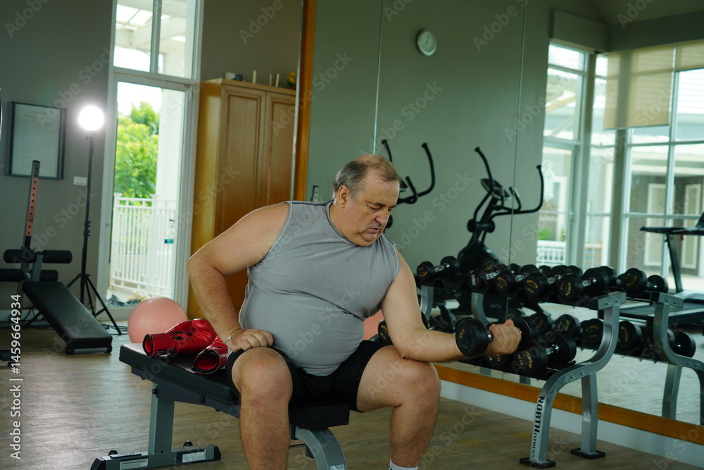 Elderly Caucasian man with a fat belly wearing gym clothes lifting dumbbells doing exercises to build muscle for health and lose weight in a fitness center Health and wellness concept