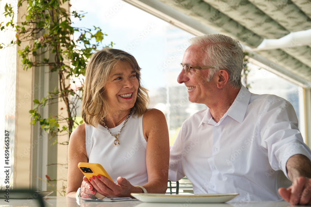 Happy retired couple talking and using mobile phone while having lunch at a restaurant