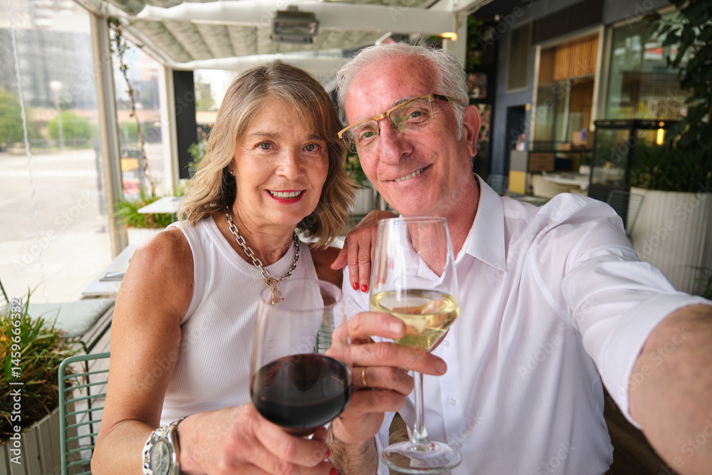 Happy retired couple taking selfie while toasting wine glasses at outdoor restaurant
