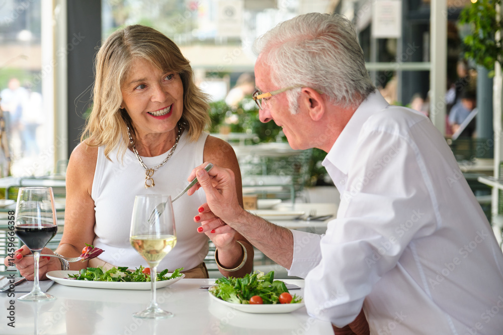 Happy mature couple eating fresh salad and drinking wine, having a pleasant conversation during their lunch date
