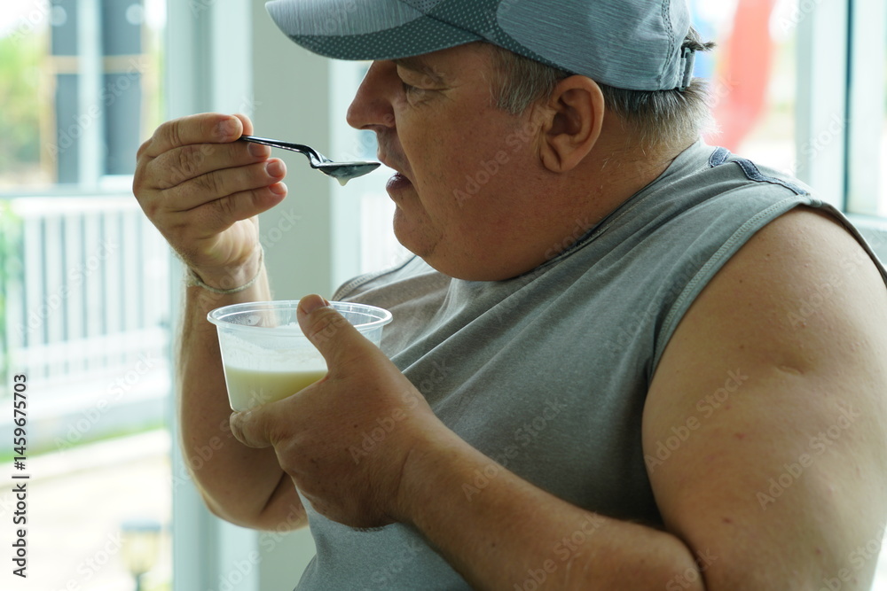 Fat Caucasian senior man with potbelly after workout hungry eating breakfast yoghurt,fruit salad healthy food and weight loss in fitness club. Health and wellness concept.