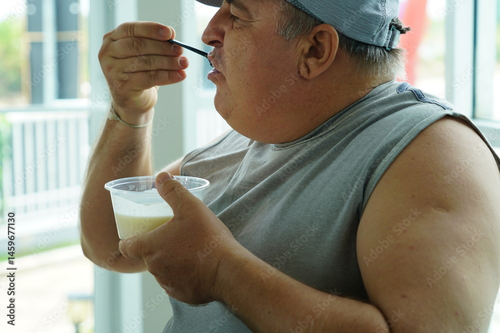 Fat Caucasian senior man with potbelly after workout hungry eating breakfast yoghurt,fruit salad healthy food and weight loss in fitness club. Health and wellness concept.
