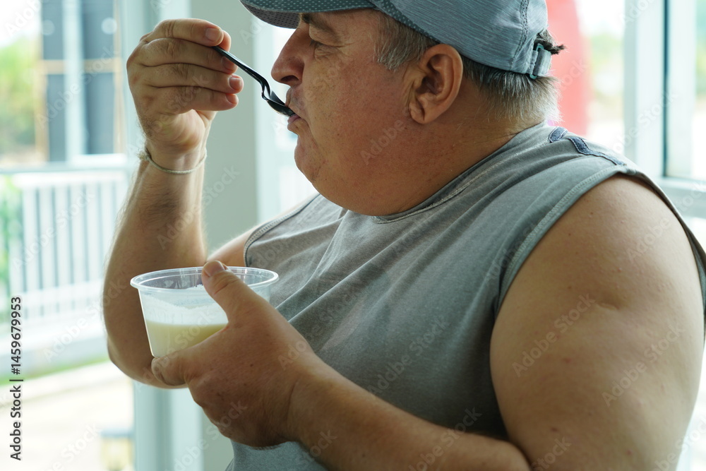 Fat Caucasian senior man with potbelly after workout hungry eating breakfast yoghurt,fruit salad healthy food and weight loss in fitness club. Health and wellness concept.