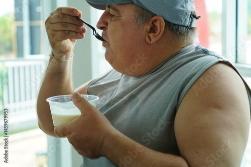 Obraz na płótnie Fat Caucasian senior man with potbelly after workout hungry eating breakfast yoghurt,fruit salad healthy food and weight loss in fitness club. Health and wellness concept. w salonie
