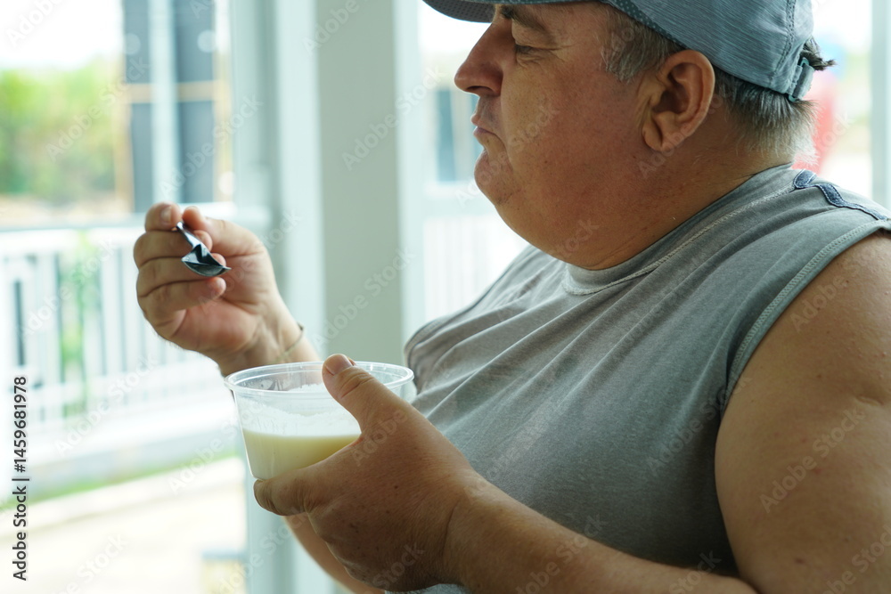 Fat Caucasian senior man with potbelly after workout hungry eating breakfast yoghurt,fruit salad healthy food and weight loss in fitness club. Health and wellness concept.
