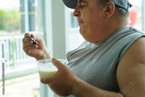 Fat Caucasian senior man with potbelly after workout hungry eating breakfast yoghurt,fruit salad healthy food and weight loss in fitness club. Health and wellness concept.