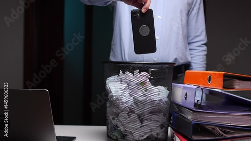 Discarding smartphone into trash bin at office desk