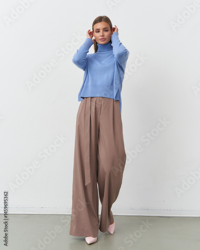 Modern fashion model poses elegantly in studio setting with chic attire and soft colors