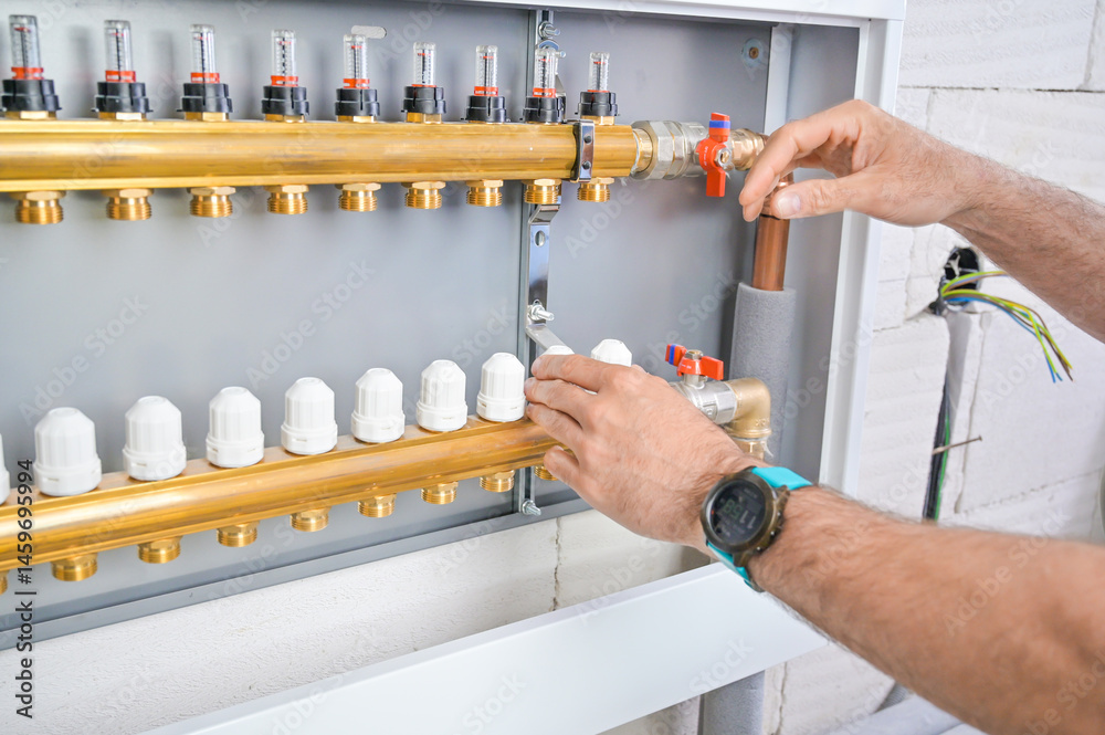 Close-up of hands adjusting valves on a plumbing system control panel, highlighting the intricate design and functionality of modern plumbing systems in residential settings