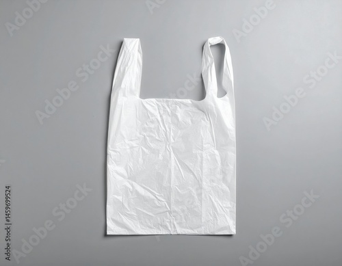 A crumpled white plastic bag rests on a textured grey background, showcasing its smooth surface and subtle creases, creating a minimalist aesthetic.