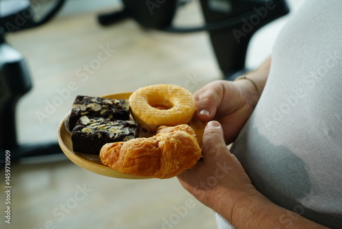 Fat man holding a tray of breakfast bread, brownies, donuts, croissants with flour and sugar.
