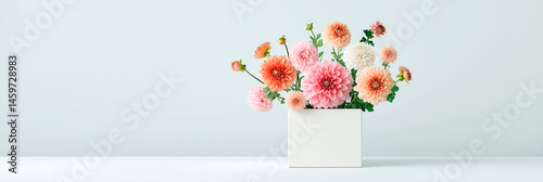 Bouquet of pastel dahlias in a white square vase on light background, arranged in a minimal and elegant composition