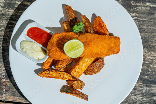Deep fried fishs and chips, served with remoulade (sauce, mustard, herbs) on white plate. Isolated by wooden table. Food Photography