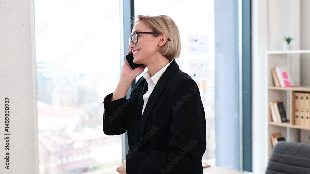 Confident woman in her 30s, dressed in formal attire, chatting on phone in stylish office setting with desk and shelves in background, conveying business success and communication Confident woman in her 30s, dressed in formal attire, chatting on phone in stylish office setting with desk and shelves in background, conveying business success and communication