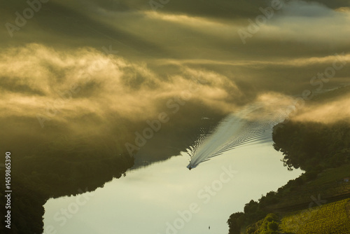 A little boat sails in Douro River on a beautiful foggy morning during the sunrise with still waters, Vila Nova de Foz Coa, Portugal.