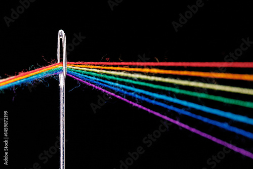 multi-colored threads for sewing in the form of a rainbow pass through an antique needle on a black background