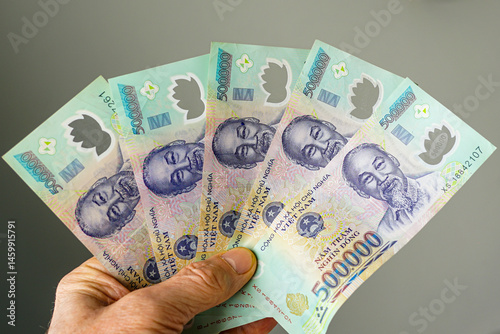 Hand holding five 500,000 dong denominations Vietnamese banknotes on a gray background