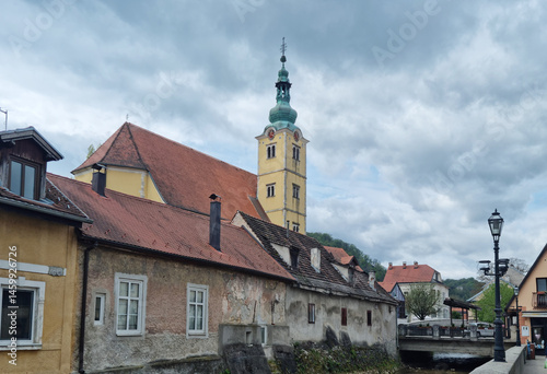 Obraz na płótnie An overcast day in Samobor showcases the steeple of St. Anastasia Church rising above charming old buildings with red-tiled roofs along a waterway w salonie