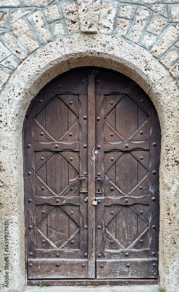 A weathered, dark wooden arched double door secured with multiple locks is set within a rustic stone archway