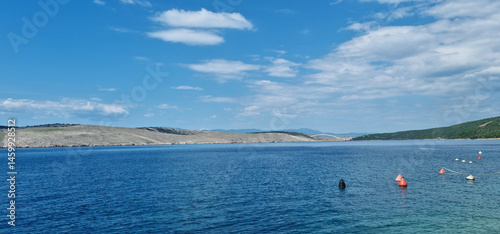 Obraz na płótnie A scenic view from Jadranovo shows the calm, deep blue Adriatic Sea leading towards the distant arch of the Krk Bridge under a partly cloudy blue sky w salonie