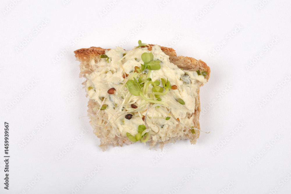 A piece of bread topped with vegan cheese spread and sprouts is isolated on a white surface
