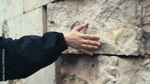 A woman's hand touches an ancient stone wall in a historic place in the city. Travel, attractions, history concept
