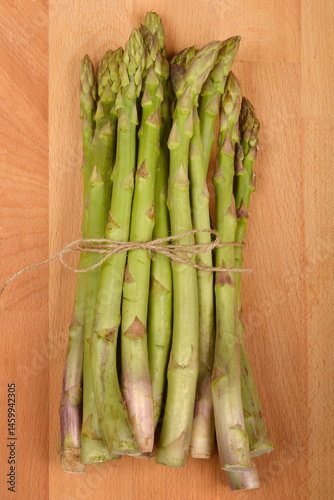 Obraz na płótnie A bundle of fresh green asparagus spears, tied together with twine, rests on a light brown wooden surface w salonie