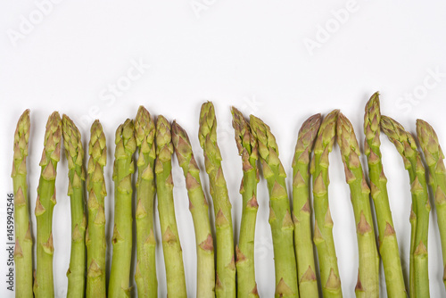Obraz na płótnie A row of fresh green asparagus spears is positioned along the bottom edge of a plain white background w salonie