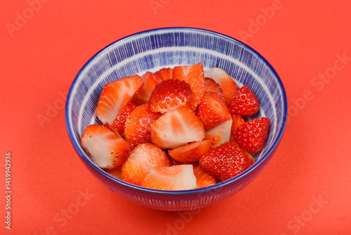 Obraz na płótnie A blue and white patterned bowl is filled with halved fresh red strawberries on a red background w salonie