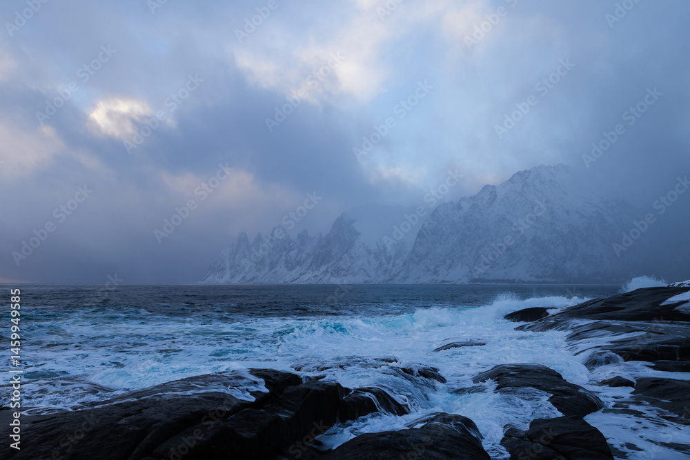 Obraz premium Okshornan auf der Insel Senja in Norwegen zur goldenen Stunde, Sturmwolken ziehen zwischen Kamera und Bergmassiv hindurch und verhüllen die Szenerie teilweise in dunklem Nebel und tiefer Struktur