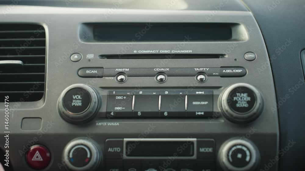 close up of car stereo system showing hand adjusting volume knob as vehicle is powered on, dashboard layout includes control buttons and CD changer with detailed focus on textures and labels close up of car stereo system showing hand adjusting volume knob as vehicle is powered on, dashboard layout includes control buttons and CD changer with detailed focus on textures and labels