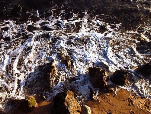 Seascape. Wild beach of Portugal. Waves in motion. Stones washed by water. Abstract background with space for insertion. Wallpaper. Postcard. Poster