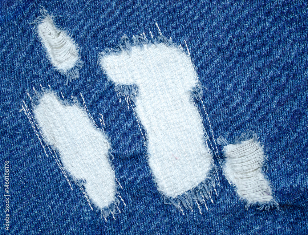 Close-up of blue denim jeans with visible white patch repair and frayed torn fabric for clothing restoration or fashion design