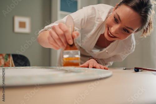 Smiling artist carefully restoring antique tabletop with gold paint