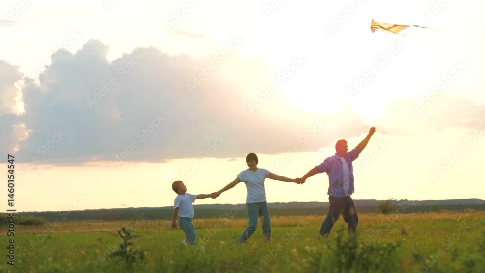 Family playing with flying kite holding hands at sunset grass wheat field outdoor leisure. Happy mother father and son relaxing enjoy freedom lifestyle weekend activity at meadow nature landscape Family playing with flying kite holding hands at sunset grass wheat field outdoor leisure. Happy mother father and son relaxing enjoy freedom lifestyle weekend activity at meadow nature landscape