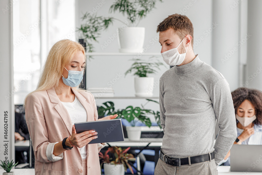 Obraz premium New normal, social distancing and boss with employee communication. Business woman in protective mask shows tablet to man, near workplace with laptop and antiseptic in interior of modern office, empty