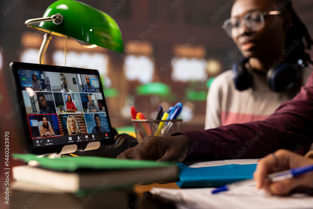 Group of diverse pupils engaging in an online course discussion via video call, participating at the remote class seminar from the campus library. Young people takes notes from academic tutor.