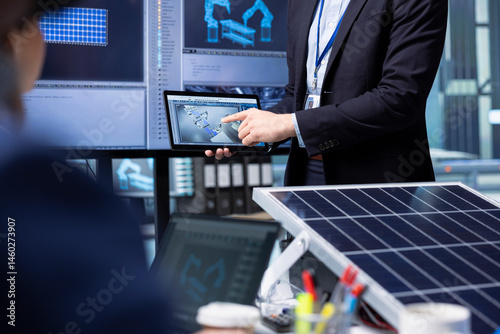 Obraz na płótnie Investors examine solar panel surface using tablet, discussing design efficiency in factory office. Businessmen holding device meeting to chat about technical improvements to solar cells, closeup w salonie