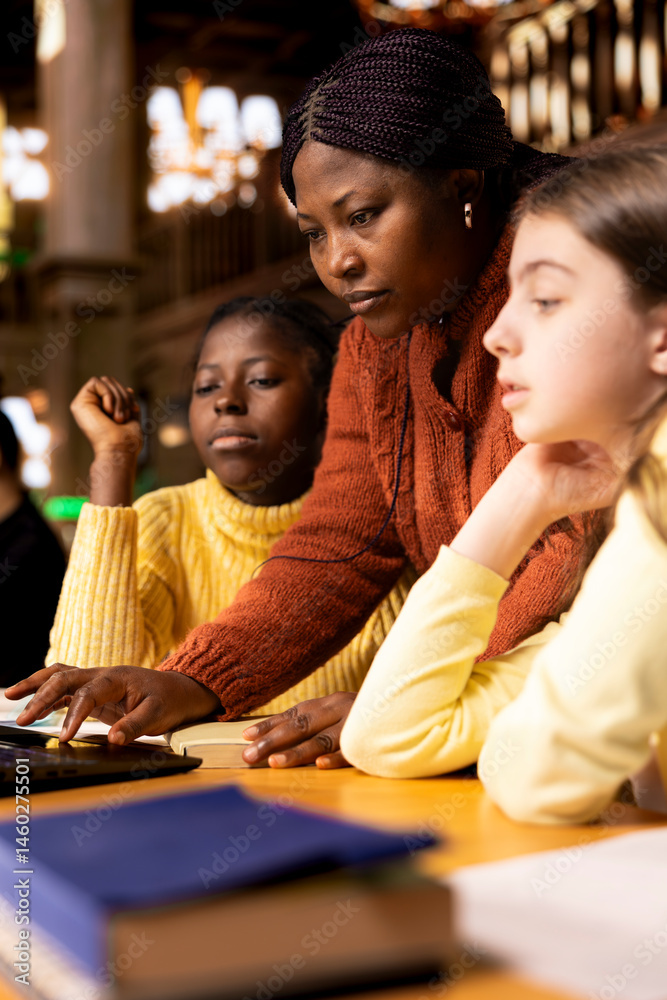 African american professor mentoring diverse students in the library, learning together in an academic library filled with curriculum books. Woman tutoring her class pupils on literature subject.