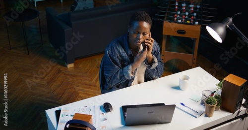 Obraz na płótnie African american teleworker receiving phone call from job colleague while working from home on laptop. Freelancer speaking with coworker using smartphone while solving tasks, camera B w salonie