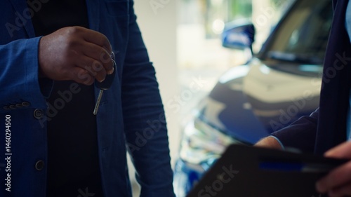 Obraz na płótnie Showroom dealer completes paperwork after selling vehicle, shaking hands with buyer and offering car keys. Salesman in dealership signing contract with man, reaching agreement, camera A close up w salonie
