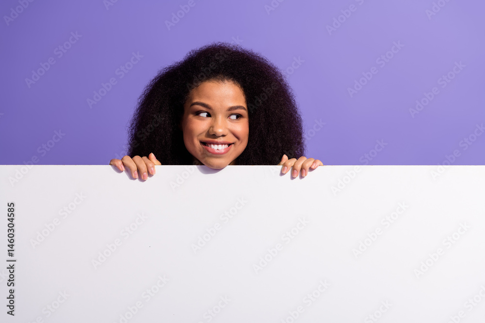 Young woman peeking over a white surface with playful expression against a solid purple background