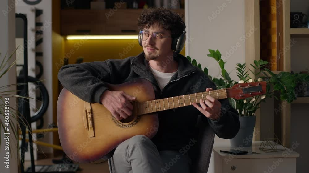 Relaxed Hispanic guitarist hipster playing acoustic guitar at home cheerful man in headphones creating melody male practicing music musician recording song guy learning play musical instrument talent