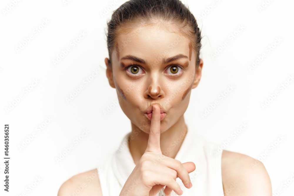 A young woman with a serious expression holds a finger to her lips, wearing a white top, evoking a sense of mystery and intrigue.