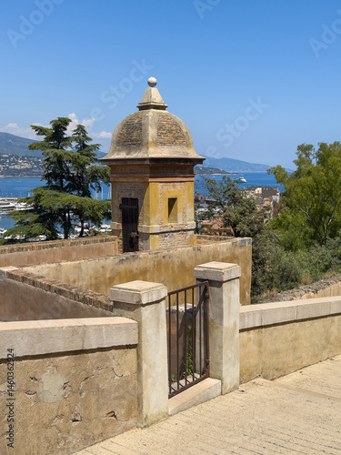 Principality of Monaco, France - July 9, 2024: Defensive tower along ramparts of Palace. Forested mountain in back under blue sky