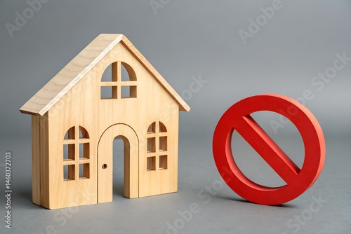 House and No Entry Sign: A wooden model house stands beside a bright red no entry sign, a symbolic representation of the concept of being unwelcome or forbidden entry.
