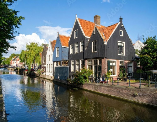 Charming canal-side houses in a Dutch town, reflecting in the tranquil water under a sunny sky.